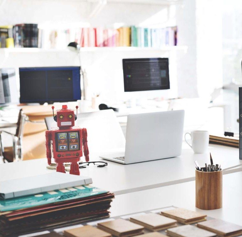 Bright studio desk with laptop, screens and a red toy robot